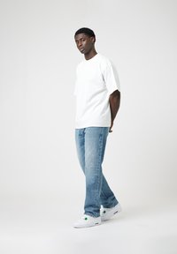 White, oversized cotton t-shirt paired with light blue denim jeans and white sneakers. Sneakers feature green accents. Simple, relaxed fit.