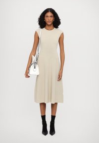 Beige ribbed knit dress with a fitted bodice and flared skirt, short sleeves, paired with a white handbag and black ankle socks with heels.