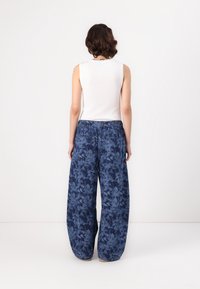Szerokie spodnie w kwiatowy wzór w ciemnoniebieskim kolorze, wykonane z lekkiego materiału, z elastycznym pasem i dwoma tylnymi kieszeniami.
