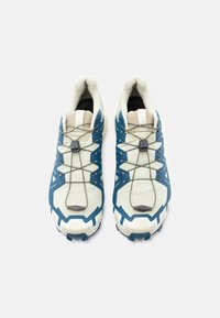 Αθλητικά παπούτσια με ανοιχτό κρεμ επάνω μέρος με μπλε λεπτομέρειες, υφασμένο πέλμα και ελαστικά κορδόνια για ασφαλή εφαρμογή. Διακριτικά γεωμετρικά σχέδια.