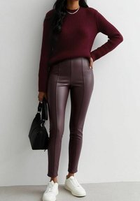 Maglione a coste color amaranto abbinato a pantaloni finti in pelle bordeaux a vita alta. Scarpe da ginnastica bianche e una borsa nera completano il look.