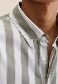 Hemd mit Kragen und vertikalen weißen und grauen Streifen, am Kragen zugeknöpft, getragen von einer Person mit mittelbrauner Haut.