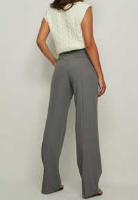 Pantalons large couleur gris clair avec une finition soignée, présentant un design ajusté, des plis à l'avant et des poches fonctionnelles.