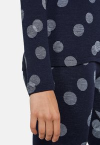 Marinblå långärmad topp med vita randiga prickar; mjuk textur; figurnära design; tydlig hand i förgrunden som visar  ärmdetaljer.