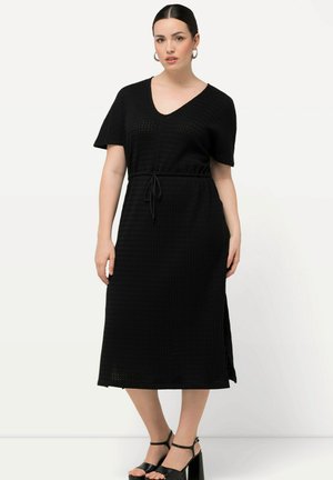 Robe midi noire à manches courtes, décolleté en V, taille à cordon, tissu texturé et fentes latérales. Assortie à des sandales noires à talons hauts.