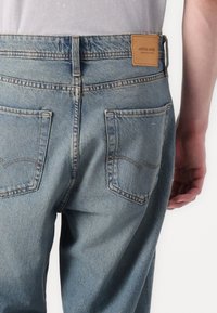 Lyseblå denim jeans med rette ben, to baklommer og et brunt lærmerke med "JACK & JONES"-merke på midjen.