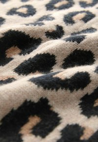 Strickstoff mit einem Leopardenmuster, das große schwarze Flecken auf einem beigefarbenen Hintergrund und kleine Pfirsichakzente zeigt, und eine weiche Textur präsentiert.
