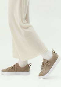 Beige mockasinsneakers med vita gummisulor, med snörning, texturerad ovandel och ljusbruna detaljer. Bärs med vita ribbade strumpor.