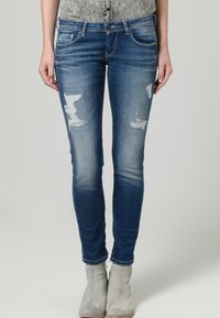 Jeans de mezclilla azul de corte slim con detalles desgastados y un ligero desteñido, que cuentan con un diseño clásico de cinco bolsillos y cierre de botón.