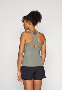 Athletisk tank topp i oliven grønn, med en stroppe-design og en utskjæring på baksiden, kombinert med svarte treningsshorts.