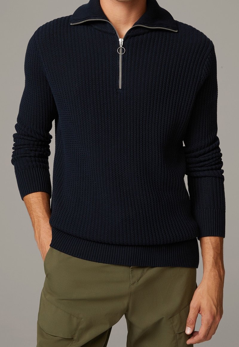 Pull en maille côtelée bleu marine avec col demi-zip et manches longues, taille ajustée et tissu texturé.