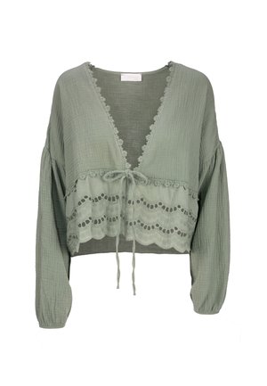 Blouse cropped à manches longues de couleur vert clair, avec un col en V, une finition en dentelle et un lien à la taille. Le tissu texturé présente un motif en forme de vagues.