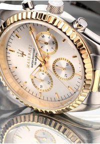 Silber und goldener Chronograph mit einem strukturierten Zifferblatt, drei Hilfszifferblättern und einer geriffelten Lünette. Wasserdicht bis 100 Meter.