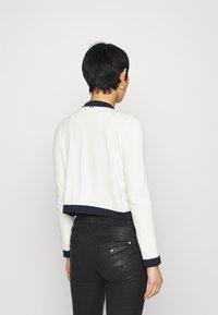 Cropped white sweater with navy trim, made of soft fabric. Features a round neck and long sleeves, worn with black slim-fit pants.
