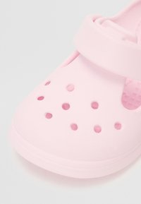 Vaaleanpunaiset muovikengät, joissa on reikiä, pyöreä kärki ja säädettävä remmi. Pintakuviointi, suunniteltu mukavuutta ja hengittävyyttä varten.