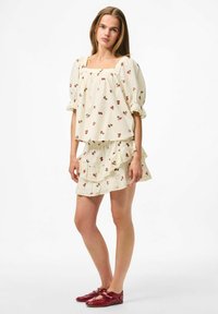 Top bianco con maniche a sbuffo e gonna coordinata con volant, stampata con ciliegie rosse, caratterizzata da scollo quadrato e bordo in pizzo. Indossato con scarpe rosse.