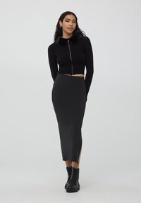 Czarny prążkowany krótki kardigan z sztucznym futerkiem, w połączeniu z elegancką czarną spódnicą midi z bocznym rozcięciem i czarnymi butami typu lace-up.