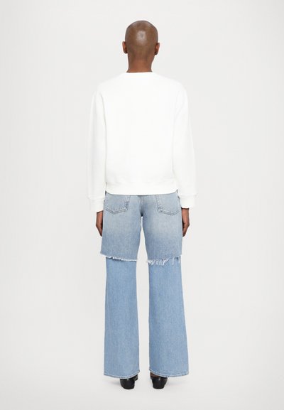 White sweatshirt with ribbed cuffs, paired with wide-leg denim jeans featuring an uneven hem and light blue gradient. Black footwear.