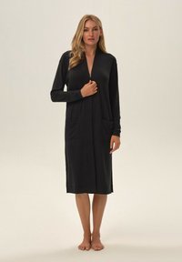Czarna sukienka z długim rękawem i głębokim dekoltem w kształcie litery V, z dwiema kieszeniami z przodu oraz prostym krojem spadającym poniżej kolan. Miękka i gładka tekstura materiału.