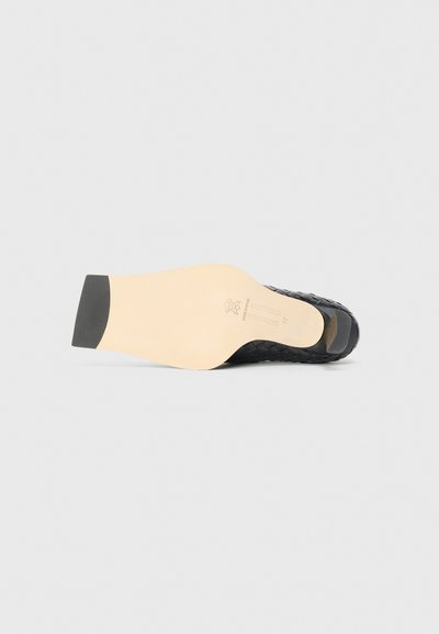 Sole di scarpa in pelle intrecciata nera con una forma caratteristica, dotata di una soletta beige liscia e un tacco in gomma per la trazione.