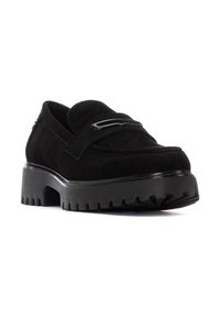 Mocasines de ante negro con una suela de goma gruesa y un dibujo rugoso, una correa decorativa en el toe y una forma de punta redondeada.