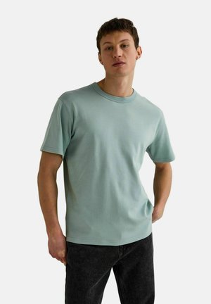 T-shirt en coton vert clair avec un col rond et des manches courtes, associée à un jean gris foncé. Texture lisse, design décontracté.