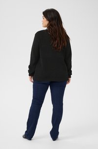 Pull noir texturé à manches longues, associé à un jean flare bleu foncé. L'accent est mis sur la vue de dos, mettant en avant la coupe et le matériau.