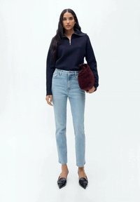 Mornarska zip-up jopica, svetlo modri ravni jeans, črne čevlje z ostro konico in temno rdeča teksturirana torbica. Preprost in sodoben outfit.