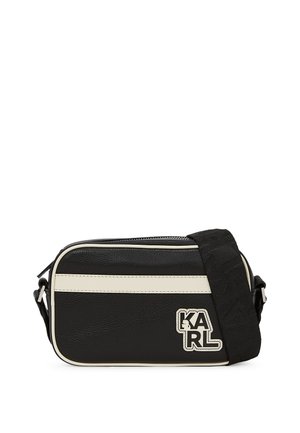 Zwarte schoudertas met een gladde textuur, voorzien van witte strepen, een logo patch en een verstelbare strap. Ritssluiting aan de bovenkant.