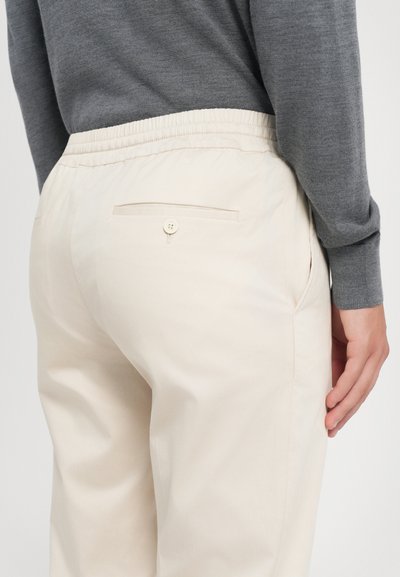 Pantaloni bej cu talie elastică, prevăzuți cu un buzunar la spate cu nasture, textură netedă și croială dreaptă.