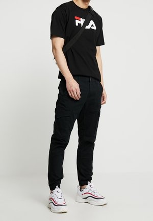 Czarny T-shirt z logo Fila, czarne spodnie typu cargo z bocznymi kieszeniami oraz białe trampki z czerwonymi akcentami. Codzienny, sportowy strój.