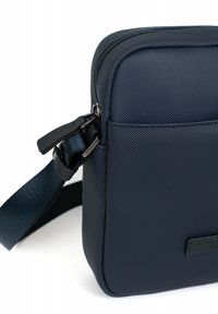 Borsa a tracolla blu navy realizzata in materiale texture, con chiusura a zip, tasca piana frontale e tracolla regolabile.