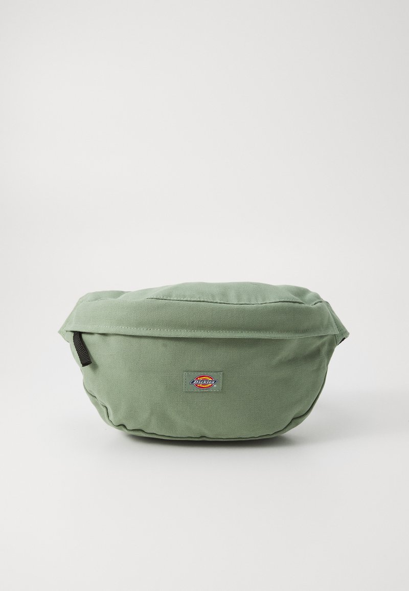 Roheline kangast kott ümmarguse kujuga, millel on esiküljel logopatch ja tõmblukuga sulgemine. Tekstureeritud kangas ja tikandite detailid.