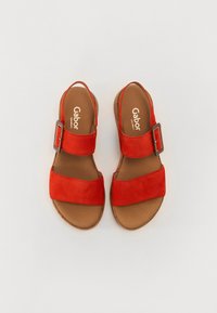 Raudoni suedes sandalai su dviem plačiomis juostelėmis ir šonine sagtimi. Rudas padas ir vidus. Minimalistinis dizainas, tinkantis kasdieniam dėvėjimui.