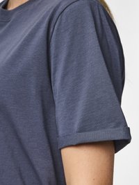 Zbliżenie osoby w koszuli z krótkim rękawem w kolorze ciemnoniebieskim ze zrolowanymi mankietami na jednolitym tle.