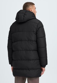 Svart dunjakke med hette, med kviltet design og elastiske ermer. Stoffet har en glatt tekstur og en middels lengde.