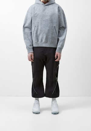 Felpa grigia a maglia con una superficie texture, dotata di tasca a marsupio. Abbinata a pantaloni cropped neri con zip e scarpe da ginnastica bianche.