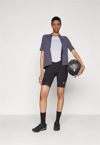 Cycling outfit featuring a navy short-sleeve jacket, white mesh underlayer, black shorts, and black cycling shoes, holding a black helmet.