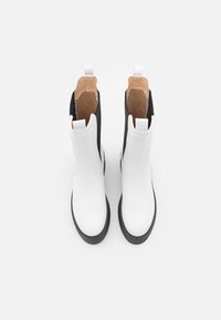 Botas brancas de tornozelo com laterais pretas, apresentando um acabamento em couro suave e interiores texturizados, pontas arredondadas e alças de puxar na parte de trás.