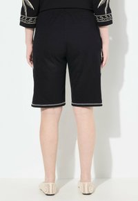 Pantaloni corti neri fino al ginocchio con elastico in vita e cuciture a contrasto. Realizzati in tessuto morbido, presentano una texture liscia e senza motivi visibili.
