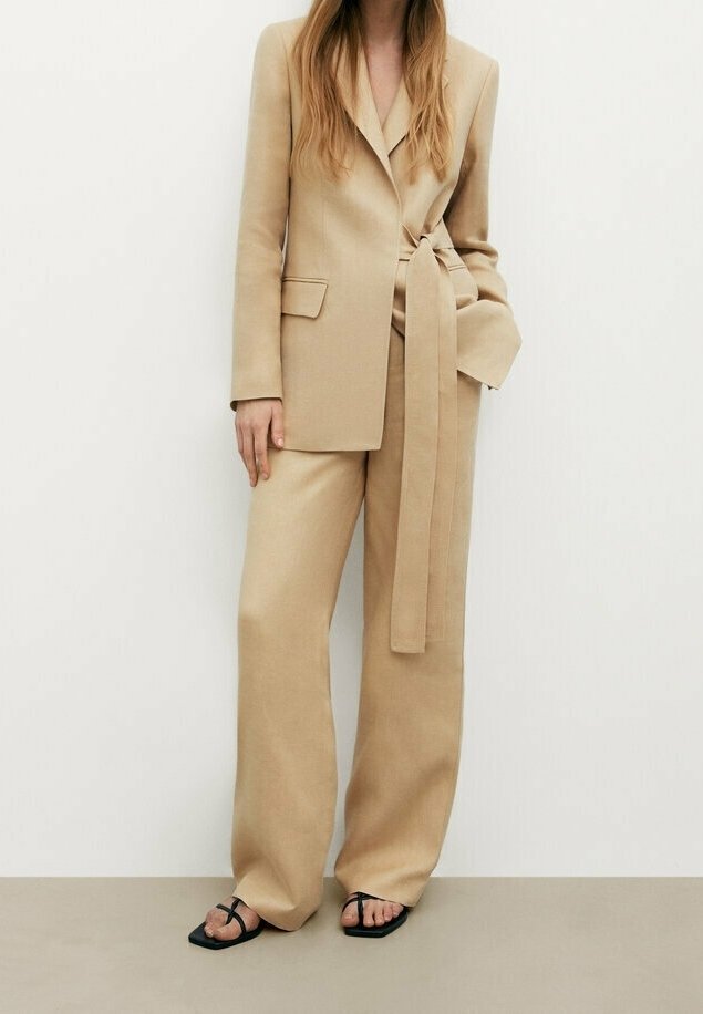 Beige skräddarsydd blazer och högmidjade vida byxor, med ett omlottbälte och mjukt tyg. Matchas med svarta sandaler.