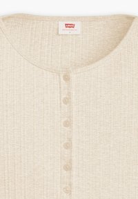 Top beige de punto acanalado con cuello redondo y seis botones en la parte delantera. Tela suave con apariencia texturizada. Etiqueta de la marca visible.