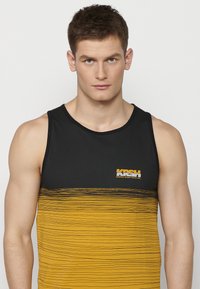 Juodas ir auksinis be rankovių marškinėliai, turintys juodą viršutinę dalį, gradientinę auksinę apatą su horizontaliomis juostelėmis ir logotipu.