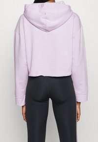 Felpa lavanda cropped con cappuccio ampio, maniche larghe e orlo a taglio vivo, abbinata a leggings neri con strisce laterali.