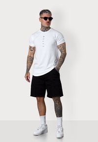 White T-shirt with vertical text, paired with black cargo shorts. Accessories include black sunglasses and white sneakers with socks.