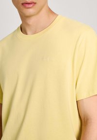 Gul bomulds T-shirt med rund hals, korte ærmer og subtilt broderet logo på brystet. Blødt tekstur med afslappet pasform.