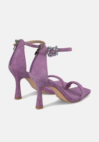 Las sandalias de tacón alto de ante morado cuentan con una cremallera en la parte trasera, una delgada correa en el tobillo y un detalle de hebilla adornada para un toque decorativo.