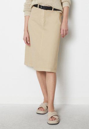 Jupe beige midi avec plis à l'avant, en tissu lisse, accompagnée d'une ceinture noire. Portée avec des sandales beiges à larges brides.