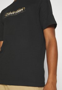 Black cotton t-shirt featuring a gold logo print across the chest. Short sleeves, crew neck, and standard fit. Smooth texture.