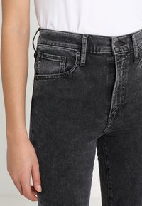Jeans de denim negro con cintura alta y pierna recta. Presentan un diseño de cinco bolsillos y un ligero desgaste, con un detalle de trabilla para cinturón visible.